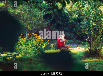 Schönheit romantische Mädchen im Freien. Schönen Teenager Modell Mädchen im roten Kleid sitzt im Garten in der Sonne Licht. Blasen, lange Haare. Sommer. Glow Sonne, S Stockfoto