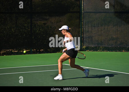 Anna Tatishvili in weißem Hemd und schwarzer Rock hits Tennis ball mit Schläger an sonnigen Green Court. Stockfoto