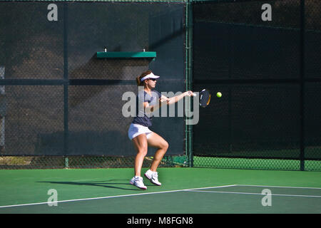 Anna Tatishvili in grauen Hemd und weißen Rock hits Tennis ball mit Schläger an sonnigen Green Court. Stockfoto