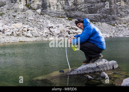 Männliche Bergsteiger in blau Daunenjacke filtern Trinkwasser aus einem See in den Anden in Peru Stockfoto
