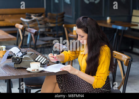 Schreiben und freiberufliche Konzept. Weibliche Writer mit langen dunklen Haaren, tragen gelbe Shirt und Polka Dot Rock, arbeiten in einem Coffee Shop, Notizen auf Stockfoto