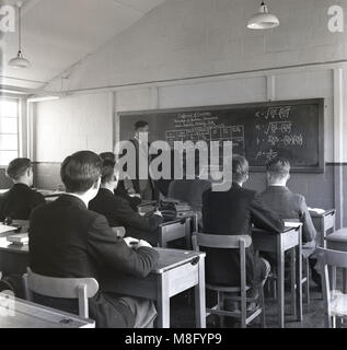 1950, historische, männliche A-Level Schüler in einem Klassenzimmer sitzen eine individuelle Holz-, statistische Messung - der Korrelationskoeffizient - durch einen männlichen Lehrer an einer Tafel Tragen eines formalen Kleid über seine Jacke, England, Grossbritannien gelehrt. Stockfoto