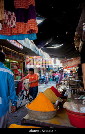 Ein Inder drückt sein Fahrrad durch besetzt Clock Tower Markt in Jodhpur Indien. Er fließt in der Nähe von einem Verkäufer mit Gewürzen. Stockfoto