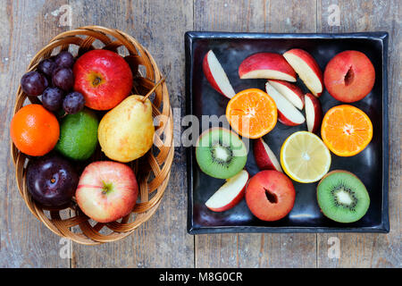 Ganze und aufgeschnittene Früchte Äpfel, Limette, Zitrone, Birnen und Pflaumen auf rustikalen Holztisch Stockfoto