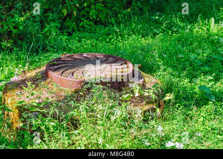 Gusseisen Abdeckung auf das Mannloch und Kanalisation Kammer unter dem grünen Gras. Stockfoto