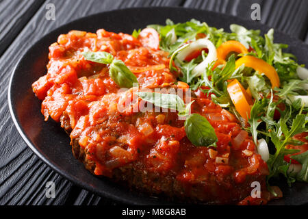 Italienischen Carne Alla Pizzaiola Fleisch und frisches Gemüse Salat close-up auf einem Teller auf den Tisch. Horizontale Stockfoto