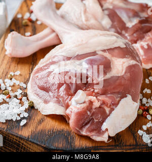 Rohes Geflügelfleisch. Entenschenkel, Knoblauch und Gewürze Salz und Pfeffer auf einem Schneidebrett. Konkreten Hintergrund. Selektiver Fokus Stockfoto