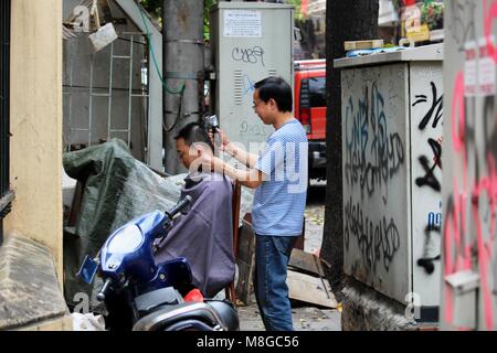 Hanoi, Vietnam - am 15. März, 2018: Lokale Straße friseur Schneiden das Haar eines Kunden auf den Straßen von Hanoi Stockfoto