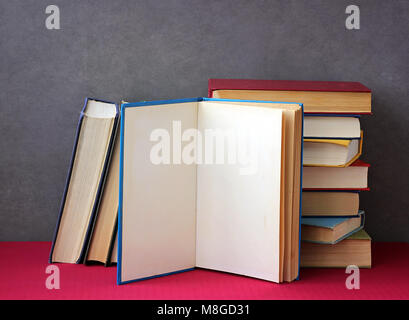 Stapel von Büchern in den farbigen Abdeckungen auf der Tabelle mit einer roten Tischdecke. Noch immer leben mit Büchern. Stockfoto