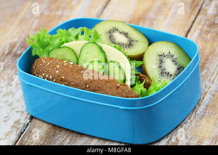 Gesunde Schule Lunch Box mit braunen Käse, Salat und Gurke roll und zwei kiwi Hälften Stockfoto