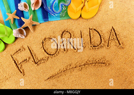 Das Wort Florida an einem Sandstrand geschrieben, mit dem Scuba Mask, Strandtuch, Seesterne und Flip Flops. Stockfoto