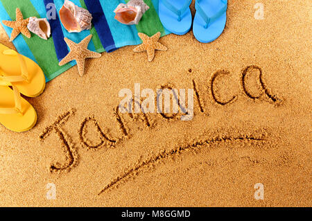 The word Jamaica written on a sandy beach, with seashells, beach towel, starfish and flip flops. Stockfoto