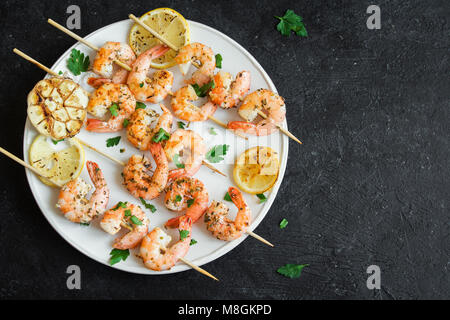 Gegrillte Garnelen Spieße. Meeresfrüchte, shelfish. Garnelen Spieße mit Gewürzen und frischen Kräutern auf Stein schwarzer Hintergrund, kopieren. Garnelen br Stockfoto