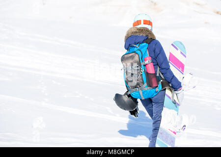 Bild von der Rückseite der Frau in Helm mit Rucksack und Snowboard Stockfoto