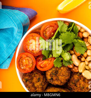 Schüssel vegetarische oder vegane Falafel Koriander Bohnen und Tomaten Buddha Schüssel gegen einen orangen Hintergrund Stockfoto