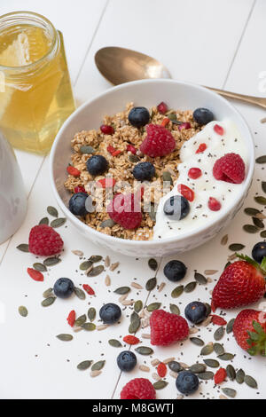 Frühstück Schüssel Müsli, Früchte, Samen, Joghurt und Honig auf einem weißen Holz Hintergrund Stockfoto