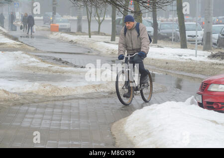 Minsk, Weißrussland - März 13, 2018: Ein älterer Mann ist, ein altes Fahrrad hinunter die Straße der Stadt. Schlechte Wetterbedingungen im Frühjahr. Starker Nebel Stockfoto