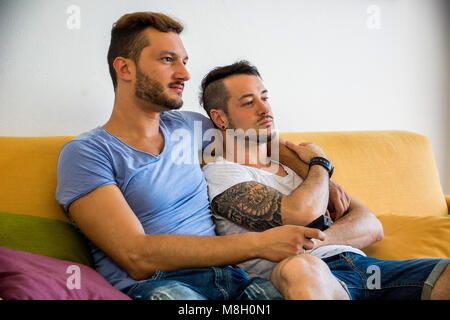 Zwei homosexuelle Männer auf dem Sofa zu Hause umarmen Stockfoto