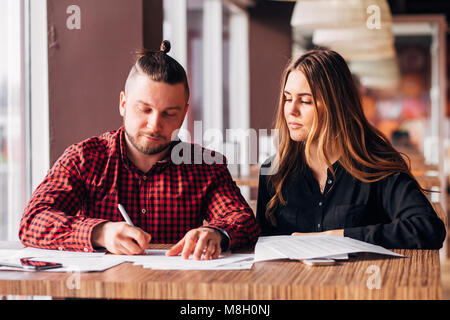 Junge Unternehmer einen Deal in ein Cafe, das Unterschreiben von Dokumenten Stockfoto