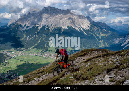 Ein Mountainbiker reitet ein Wanderweg oberhalb der österreichischen Stadt Lermoos mit der Zugspitze im Hintergrund. Stockfoto