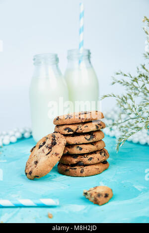 Cookie Schokolade mit einem organischen Milchflaschen in der Nähe von Blüten auf blauem Hintergrund. Gesundes Frühstück Konzept. Minimalistisch. Frühling Essen. Stockfoto