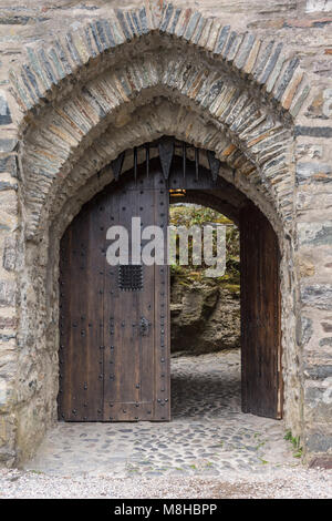 Dornie, Schottland - Juni 10, 2012: Nahaufnahme von Grau-Stein verbeugte sich Eingang zum Eilean Donan Castle. Braune Tür geöffnet und zeigt einige grüne Vegetation. Stockfoto