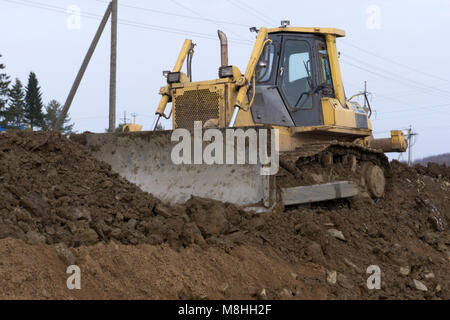 Die gelbe Traktor mit angehängtem grederom macht Boden ausrichten. Die Arbeiten an der Kanalisation im Bereich Stockfoto