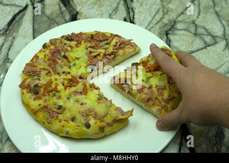 Nahaufnahme von Frau handpflückung Scheibe Mozzarella cheesy Pizza auf Holz- pan zu Hause. Hausgemachte Pizza Stockfoto