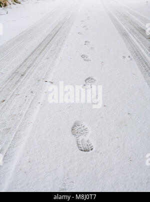 East Lothian, Schottland, Großbritannien, 18. März 2018. Schnee als Folge eines kalten Wetters. Verschneite Fußabdrücke und Reifenspuren auf einer schneebedeckten Straße Stockfoto