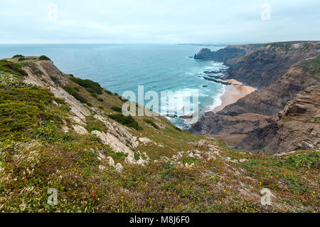 Sandstrand mit felsigen Bergrücken trübes Wetter Aussicht auf Sommer Atlantic an der felsigen Küste (Costa Vicentina, Algarve, Portugal). Und Ocean Surf Wellen. Stockfoto