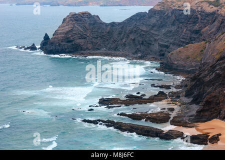 Sandstrand mit felsigen Bergrücken trübes Wetter Aussicht auf Sommer Atlantic an der felsigen Küste (Costa Vicentina, Algarve, Portugal). Und Ocean Surf Wellen. Stockfoto