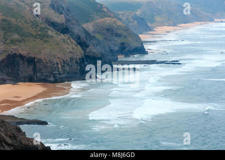 Sandstrand mit felsigen Bergrücken trübes Wetter Aussicht auf Sommer Atlantic an der felsigen Küste (Costa Vicentina, Algarve, Portugal). Und Ocean Surf Wellen. Stockfoto