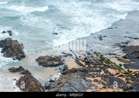 Sandstrand mit felsigen Bergrücken trübes Wetter Aussicht auf Sommer Atlantic an der felsigen Küste (Costa Vicentina, Algarve, Portugal). Und Ocean Surf Wellen. Stockfoto