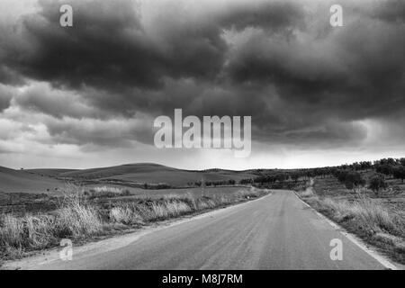 Lonely Kunst Natur Hügel auf der grünen Wiese und Asphalt unter bewölktem Himmel stürmisches Wetter Schwarz/Weiß-Bild Stockfoto