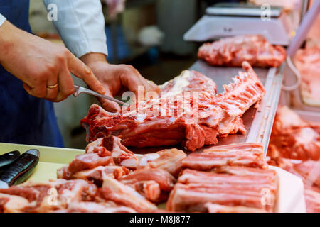 Zugeschnittenes Bild der männlichen Metzger schneiden von rohem Fleisch mit Messer an der Theke im Shop Stockfoto