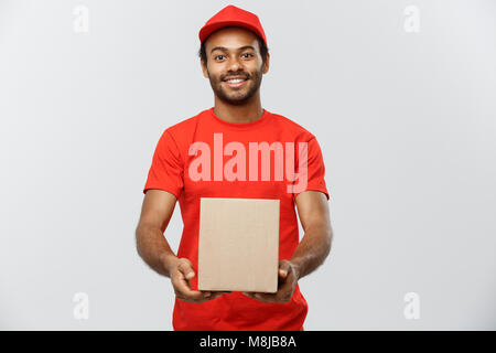 Lieferung Konzept - Portrait von Happy African American Lieferung Mann im roten Tuch Holding eine Box Paket. Auf Grau studio Hintergrund isoliert. Kopieren Sie Platz. Stockfoto