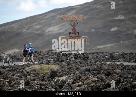 Die Statue "El Diablo" von César Manrique, und zwei Radfahrer in Parque Nacional de Timanfaya, Nationalpark Timanfaya auf Lanzarote ruhen Stockfoto