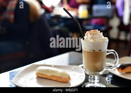 Kaffee mit Sahne und Eclair auf dem Tisch in einem Cafe Stockfoto