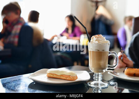 Kaffee mit Sahne und Eclair auf dem Tisch in einem Cafe Stockfoto