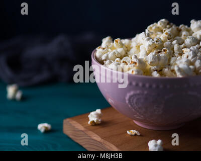 In rosa Schüssel auf Holzbrett Popcorn auf dunklem Hintergrund Stockfoto