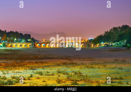 Die angenehmen Abendspaziergang in Moshtagh-e Aval Park mit Blick auf den Fluss Zayandeh ausgetrocknet und gewölbte Joui Brücke, Isfahan, Iran. Stockfoto