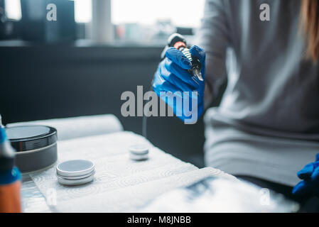 Weibliche Tätowierer in Blau sterile Handschuhe hält Tattoo Maschine in der Hand, professionelle Tätowierer tools. Tattooing in Salon Stockfoto