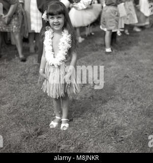 1950er Jahre, historische Bild, eine glückliche kleine Mädchen stehen eine Fete lächelnd, stolz ihr Kostüm einer hula oder Gras Rock mit Blume Halskette in einem childrens Fancy Dress Wettbewerb tragen. Stockfoto