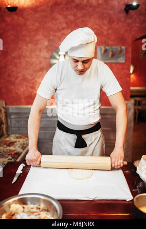 Männliche Chef rollen Sie den Teig mit einem Nudelholz auf hölzernen Tisch. Hausgemachte Strudel kochen Stockfoto