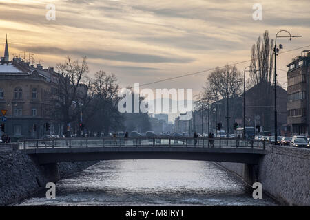 SARAJEVO, BOSNIEN - 17. FEBRUAR 2018: Fußgänger Passieren einer Brücke über den Fluss Miljacka in Sarajewo bei Sonnenuntergang. Miljacka ist einer der beiden Flüsse o Stockfoto