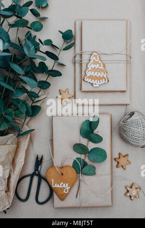 Verpackung Weihnachtsgeschenke mit Normalpapier und Lebkuchen Plätzchen mit Puderzucker auf ihnen Stockfoto