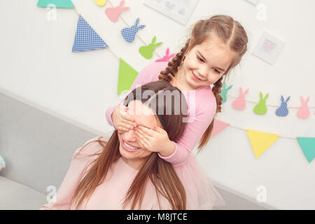 Junge Mutter und Tochter gemeinsam Wochenende zu Hause Mädchen schließen die Augen der Mutter eine Überraschung Stockfoto