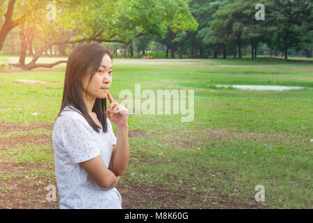 Und Urlaub Konzept: Frau tragen weiße T-Shirt. Sie stehen auf grünem Gras im Park und etwas denken. Stockfoto