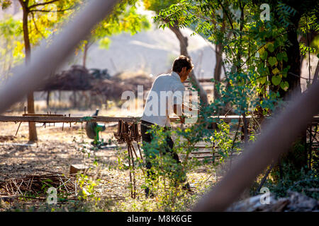 Ein hübscher junger Mann ist Arbeiten im Freien im indischen Dorf Nipal, biegen Eisenstangen während der schönen sonnigen Tag unter Bäumen. Das Licht ist golden warm wie Stockfoto