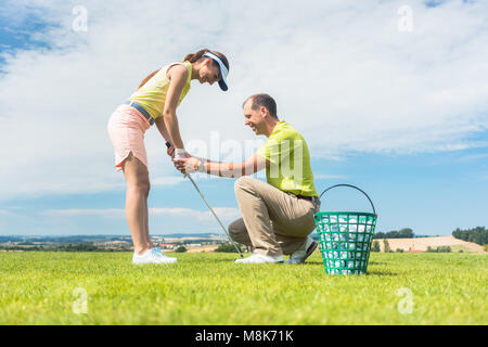 Junge Frau die Ausübung des Golf schwingen Sie durch Ihr Ausbilder half Stockfoto